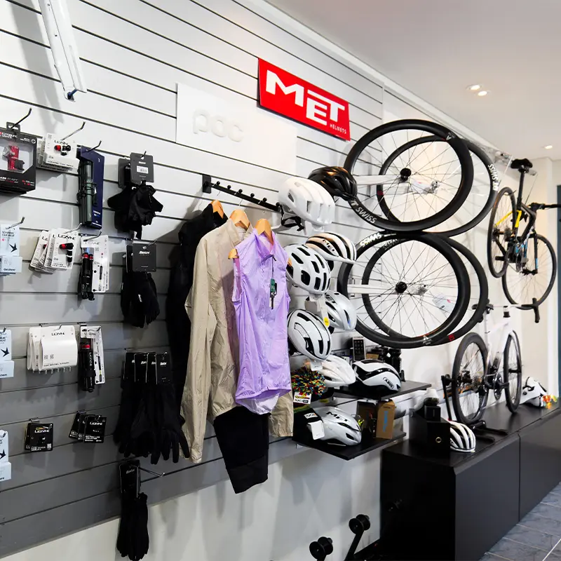 A bike shop retail wall displays MET helmets, cycling apparel, gloves, and carbon wheels.
