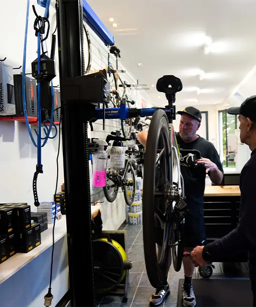 A mechanic services a road bike on a repair stand inside a bike shop.